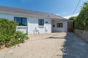 A single-story house with a paved driveway, a wooden gate, and a small garden area with flowering plants. - 4 Bed in Trevone (oc-p00696) (Trevone)