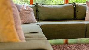 A green sofa with cushions, a window with a view of greenery, and a wooden floor. - 2 Bed in Tresarrett (oc-b34255) (Blisland)