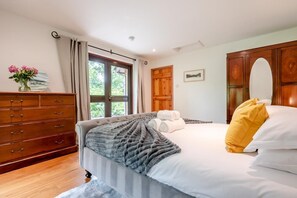 A bedroom with a bed, a wooden dresser, a window with curtains, and a door.