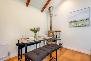 A cozy dining area with a bench, a table set for two, and a wood-burning stove.