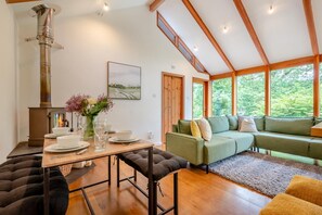 A cozy living room with a green sofa, a wooden table set for dining, and a wood-burning stove. - 2 Bed in Tresarrett (oc-b34255) (Blisland)