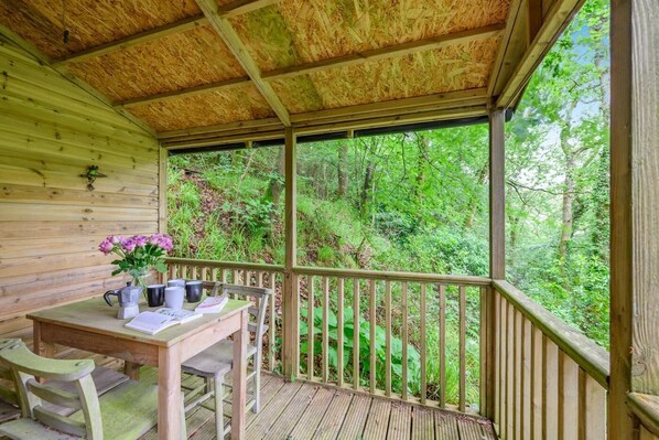 A wooden deck with a table and chairs, a coffee maker, and a vase of flowers.
