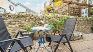 Un espace patio avec des sièges d’extérieur, une table avec un journal et un mur de pierres en arrière-plan.
