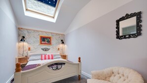 Une chambre à coucher comprenant un lit, deux lampes de chevet, une table de chevet, une chaise, un mur décoré d’une carte, un miroir et une lucarne.