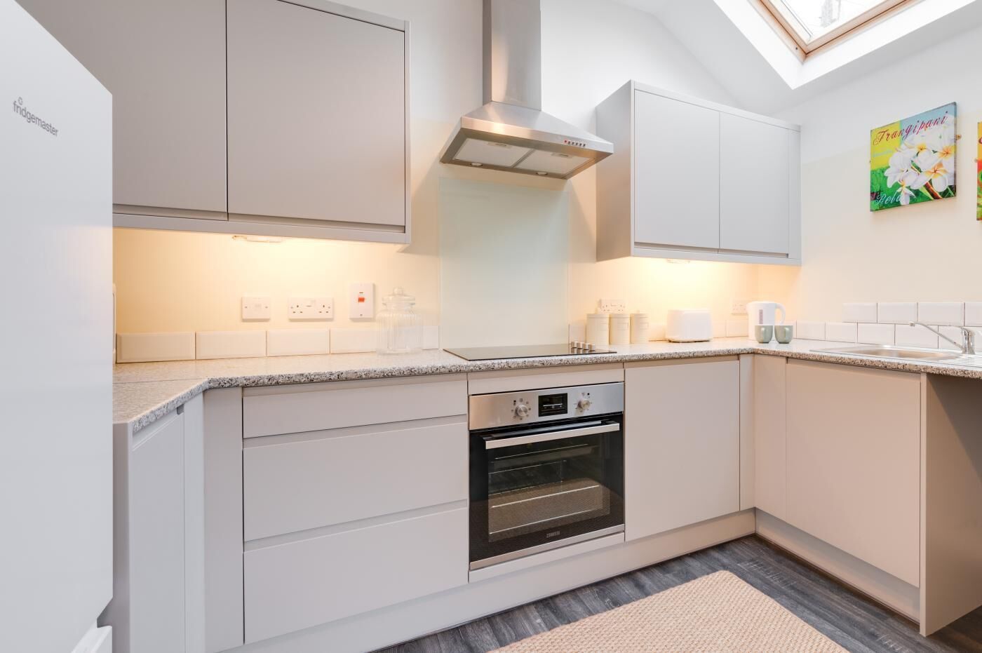 A modern kitchen with white cabinetry, a built-in oven, and a skylight.