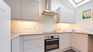 Une cuisine moderne avec des meubles blancs, un four encastré et une lucarne.