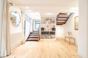 A spacious hallway with wooden flooring, a built-in bookshelf, a mirror, and a staircase. - 4 Bed in Tresarrett (oc-b34254) (Blisland)