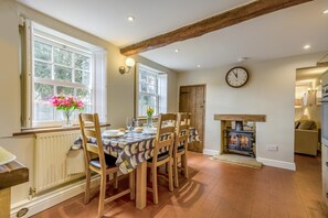 Un coin repas avec une table en bois, des chaises, une horloge et une cheminée.