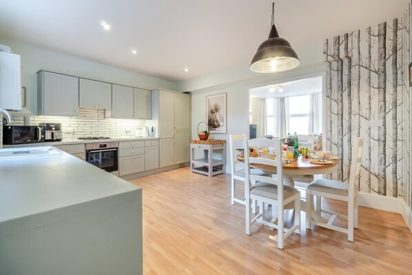 A modern kitchen with a central island, white cabinetry, and a dining area with a wooden table and chairs.