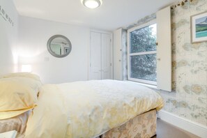 A bedroom with a bed, a round mirror, a white door, and a window with a view of trees.