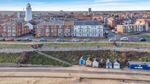 A coastal town with a prominent lighthouse, terraced houses, and a promenade with colorful beach huts.