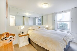 A bedroom with a bed, bedside lamps, a wooden nightstand, a mirror, and a window.