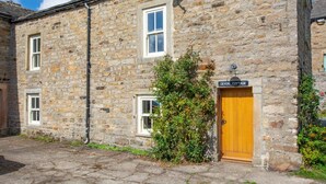 A stone cottage with a wooden door, a satellite dish, and a sign reading "Devon Cottage". - 2 Bed in Gunnerside (oc-ds1068) (Gunnerside)