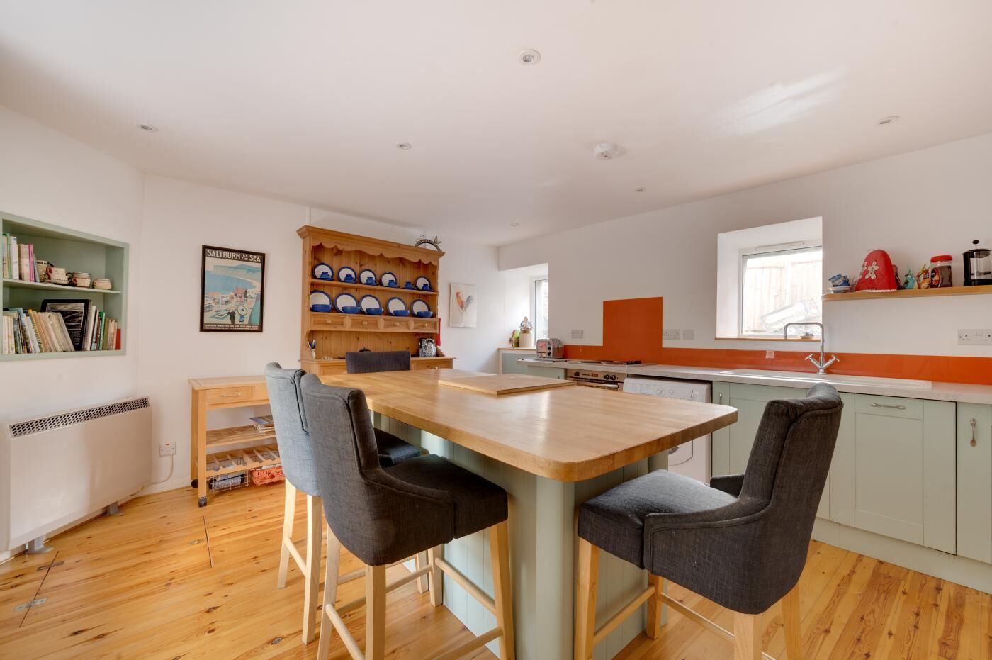 Une cuisine moderne avec une table et des chaises en bois, une bibliothèque et une fenêtre.