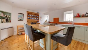 A modern kitchen with a wooden table and chairs, a bookshelf, and a window. - 2 Bed in Gunnerside (oc-ds1068) (Gunnerside)