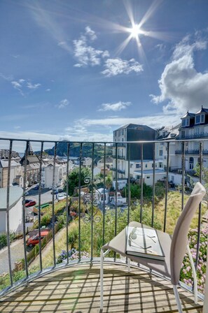 Ein Balkon mit einem Stuhl, einem Glastisch und Blick auf Gebäude und Grünflächen.
