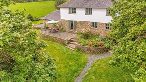 A white house with a stone exterior, a patio with outdoor furniture, and a garden. - 4 Bed in Helford (oc-s34375) (Helford)