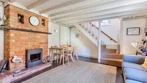 Un salon avec une cheminée en briques, un coin repas, un escalier et un canapé bleu.