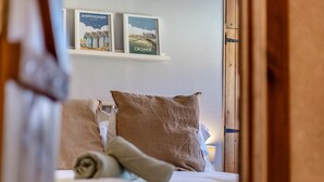Une chambre à coucher avec un lit, des oreillers et une étagère fixée au mur, ornée de tableaux encadrés.