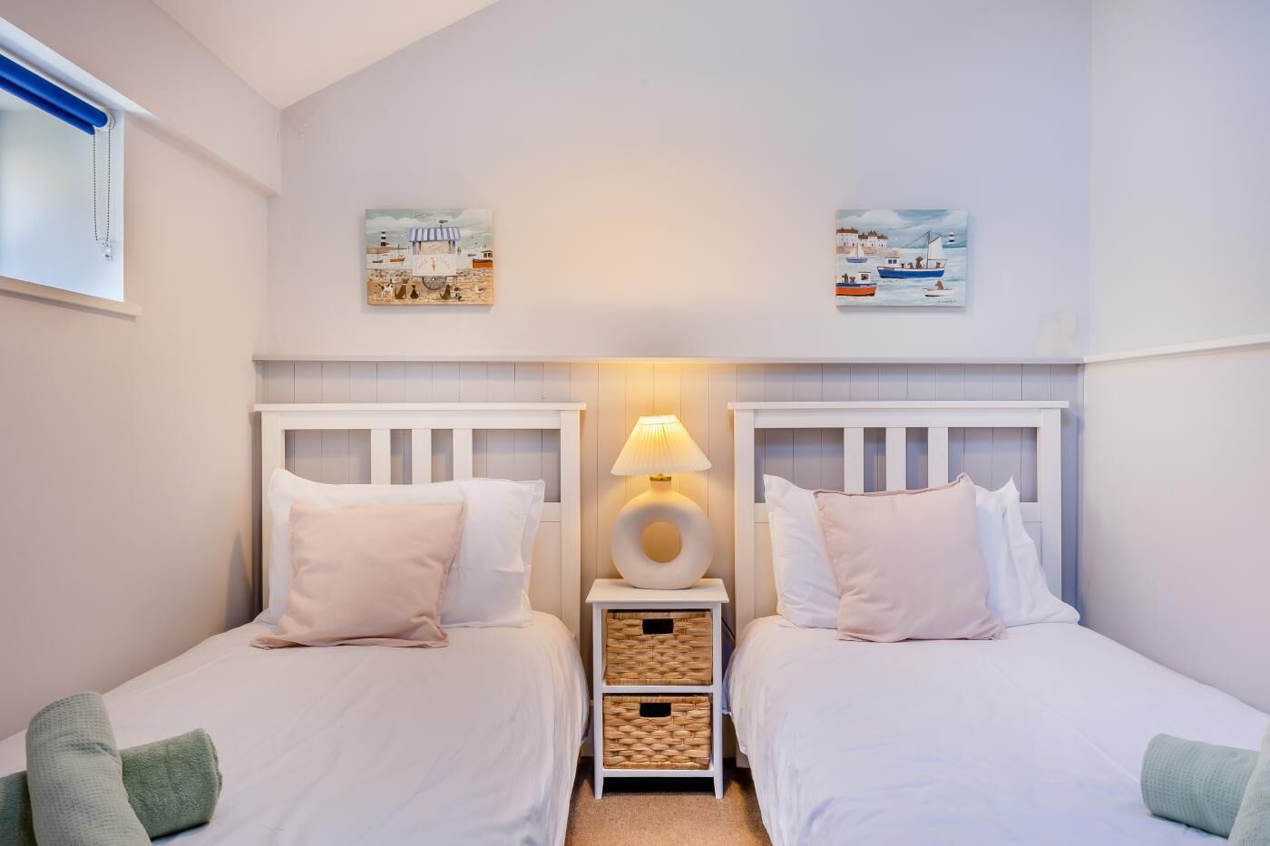 A bedroom with two beds, a bedside lamp, and two wall-mounted artworks.