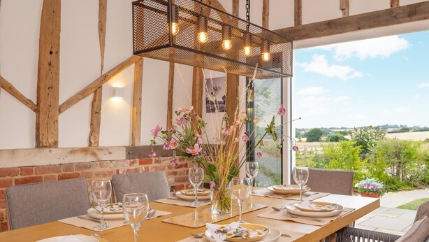 Een terras met een houten tafel gedekt voor een maaltijd, omringd door stoelen en een hanglamp erboven.