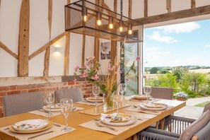 Un espace de restauration en plein air avec une table en bois dressée pour un repas, entourée de chaises, et un luminaire suspendu au-dessus.