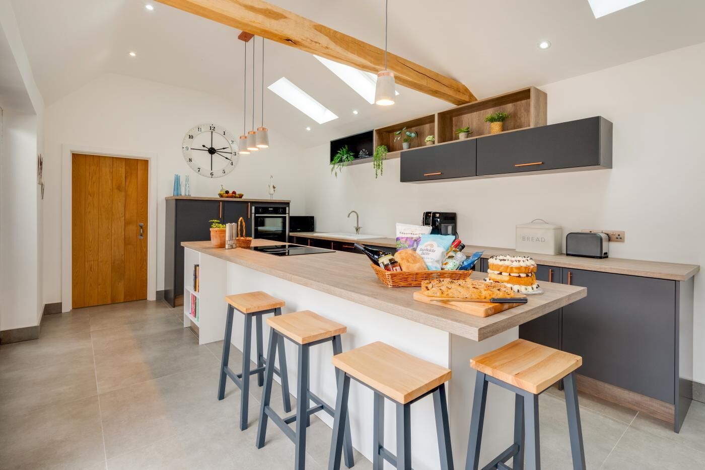 Una cocina moderna con una isla central, taburetes de bar, un reloj y estantes empotrados con plantas.