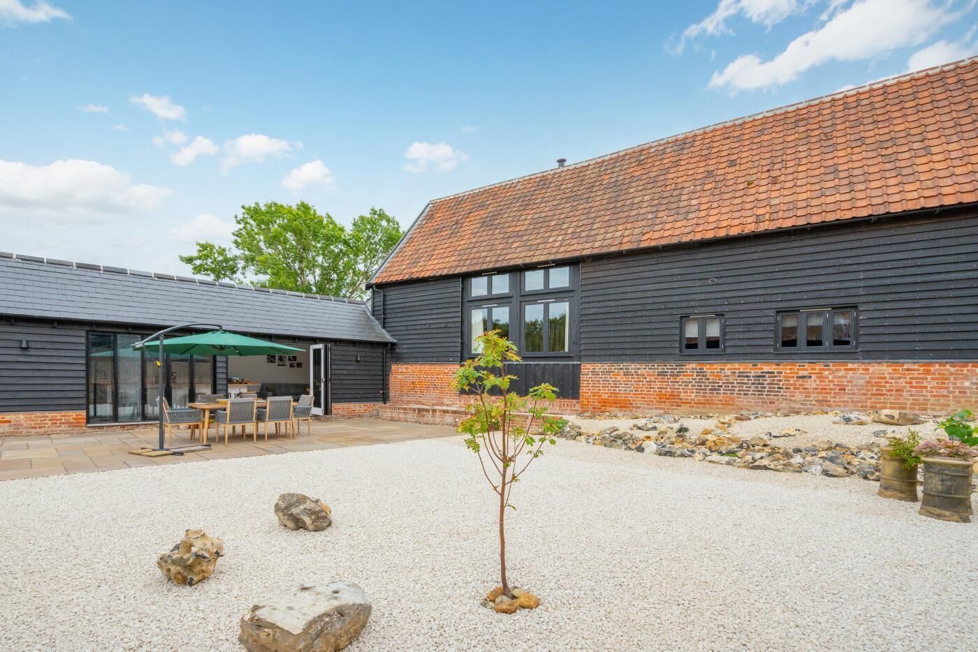A building with a gravel courtyard, a covered outdoor seating area, and a small tree.