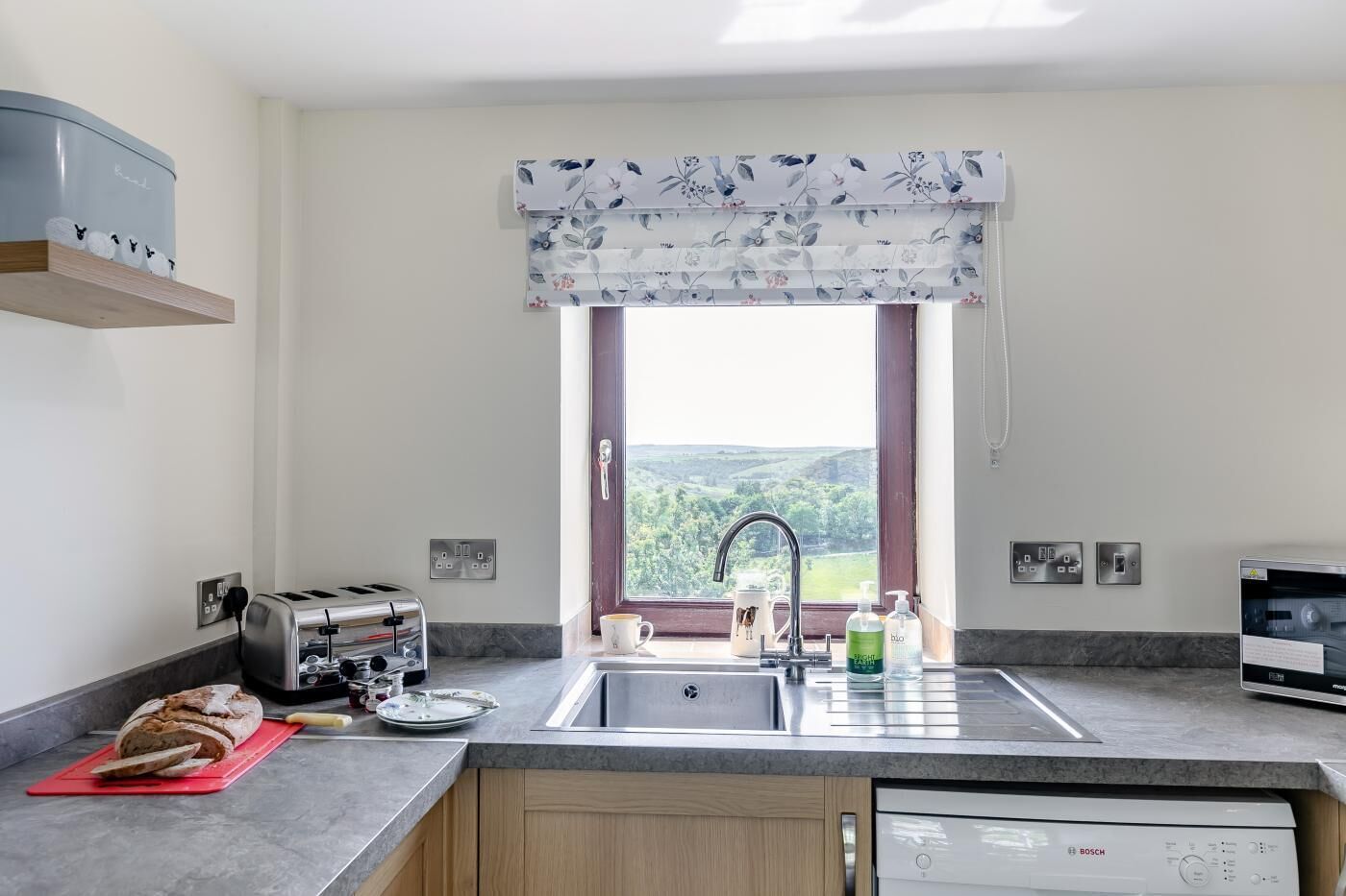 A kitchen with a toaster, a bread loaf, a sink, and a Bosch dishwasher.