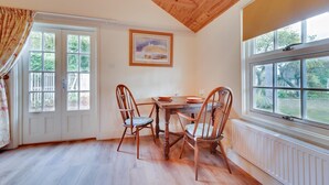 Un comedor con mesa y sillas de madera, una ventana con vistas a la vegetación y una puerta con vista a una cerca de madera.