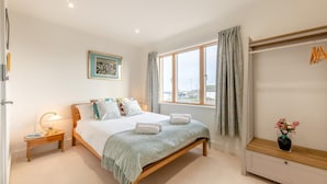 Een slaapkamer met een bed, nachtkastje, raam en een kledingkast.
