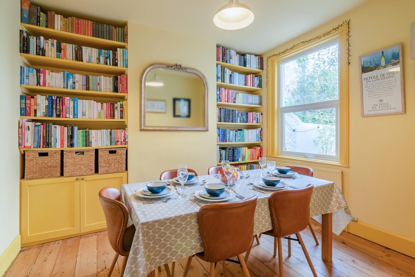 Un comedor con una mesa dispuesta para cuatro personas, rodeado de estanterías, un espejo y una ventana con vistas.