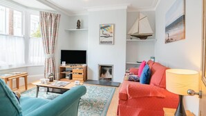 A living room with a TV, sofa, armchair, and a fireplace. - 3 Bed in Brighton (oc-bt004) (Hove)