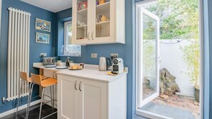 A kitchen with a white countertop, a coffee maker, and a toaster. There is a window with a view of greenery outside. - 3 Bed in Brighton (oc-bt004) (Hove)