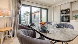 Un comedor moderno con una mesa de mármol, sillas tapizadas en gris y un amplio ventanal con cortinas.