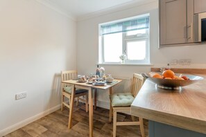 Una cocina con una mesa de comedor, sillas, un cuenco de fruta y una ventana con persianas.