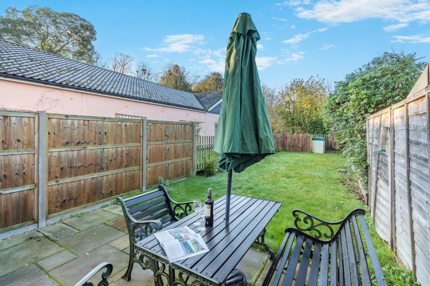 A patio with a table, two chairs, a green umbrella, and a wooden fence.