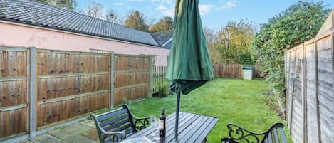 A patio with a table, two chairs, a green umbrella, and a wooden fence.