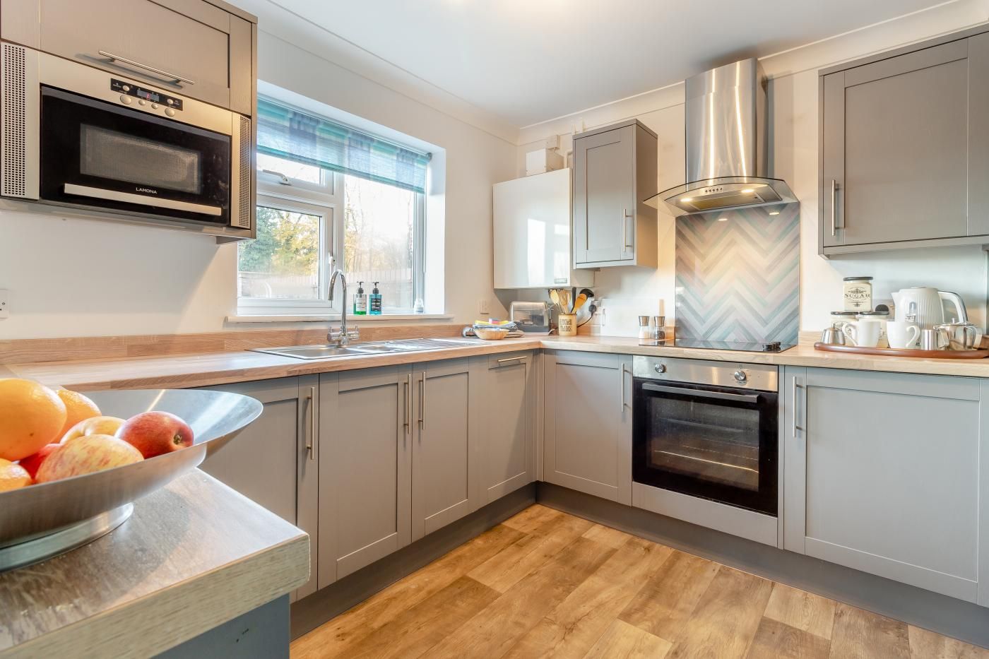 A modern kitchen with stainless steel appliances, a large window, and a herringbone-patterned backsplash.