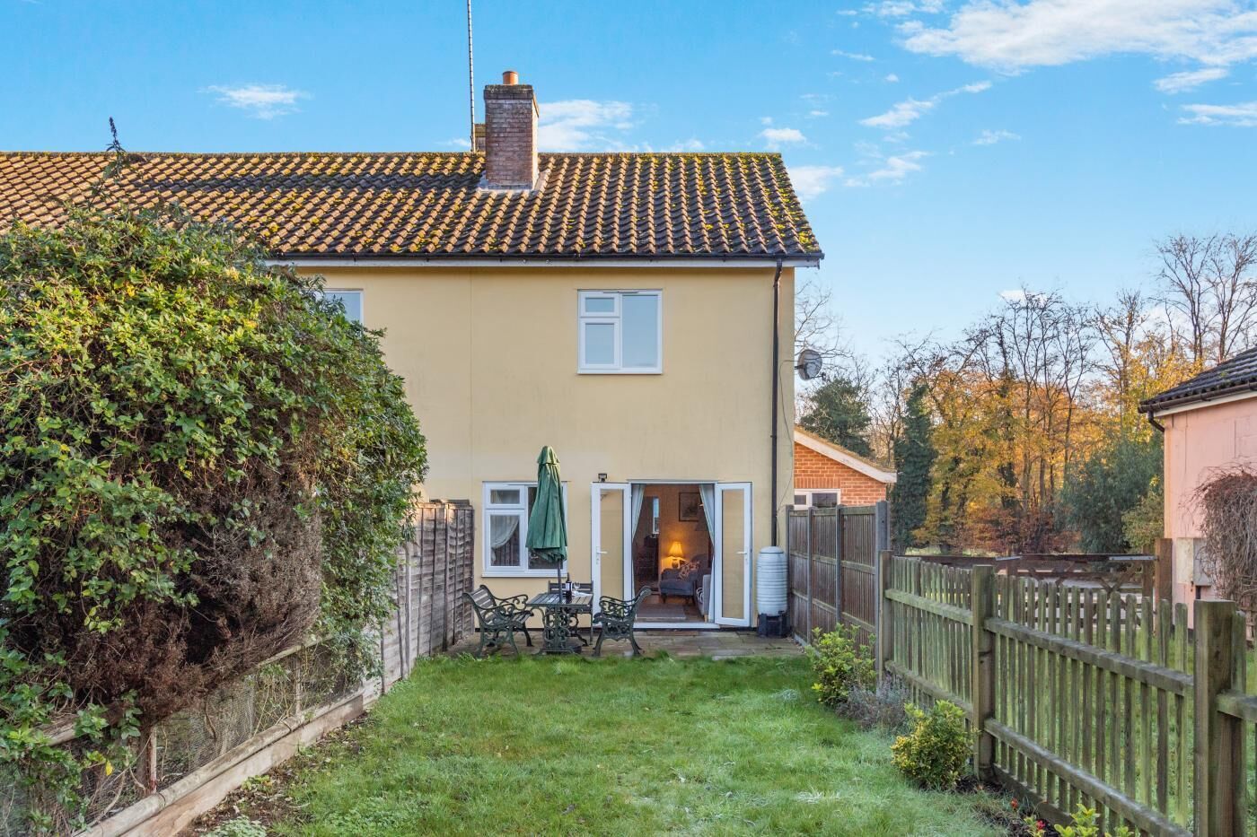 A two-story house with a tiled roof, a visible chimney, and a small garden area with a wooden fence.