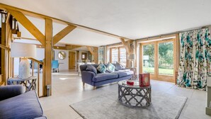 A spacious living room with a blue sofa, a coffee table, and a view of the outdoors through large windows. - 2 Bed in Holmbury St. Mary (oc-midfb) (Holmbury Saint Mary)