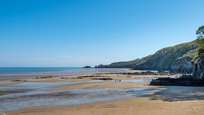 Ein Strand mit blauem Himmel, felsigen Klippen und ruhigem Wasser.