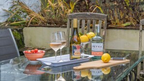 A glass table with a bottle of Reyka vodka, two wine glasses, a bowl of cherry tomatoes, and a lemon on a wooden cutting board. - 3 Bed in Trellech (oc-j34206) (Trelleck)