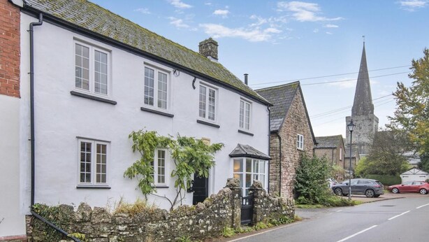A white building with multiple windows, a stone wall, and a church steeple in the background. - 3 Bed in Trellech (oc-j34206) (Trelleck)