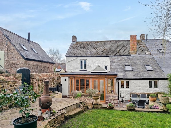 A stone house with a garden patio, a chimney, and a large pot.