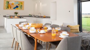 Un espace repas moderne avec une table en bois mise pour le petit-déjeuner, une cuisine en arrière-plan et une vue sur l’extérieur.