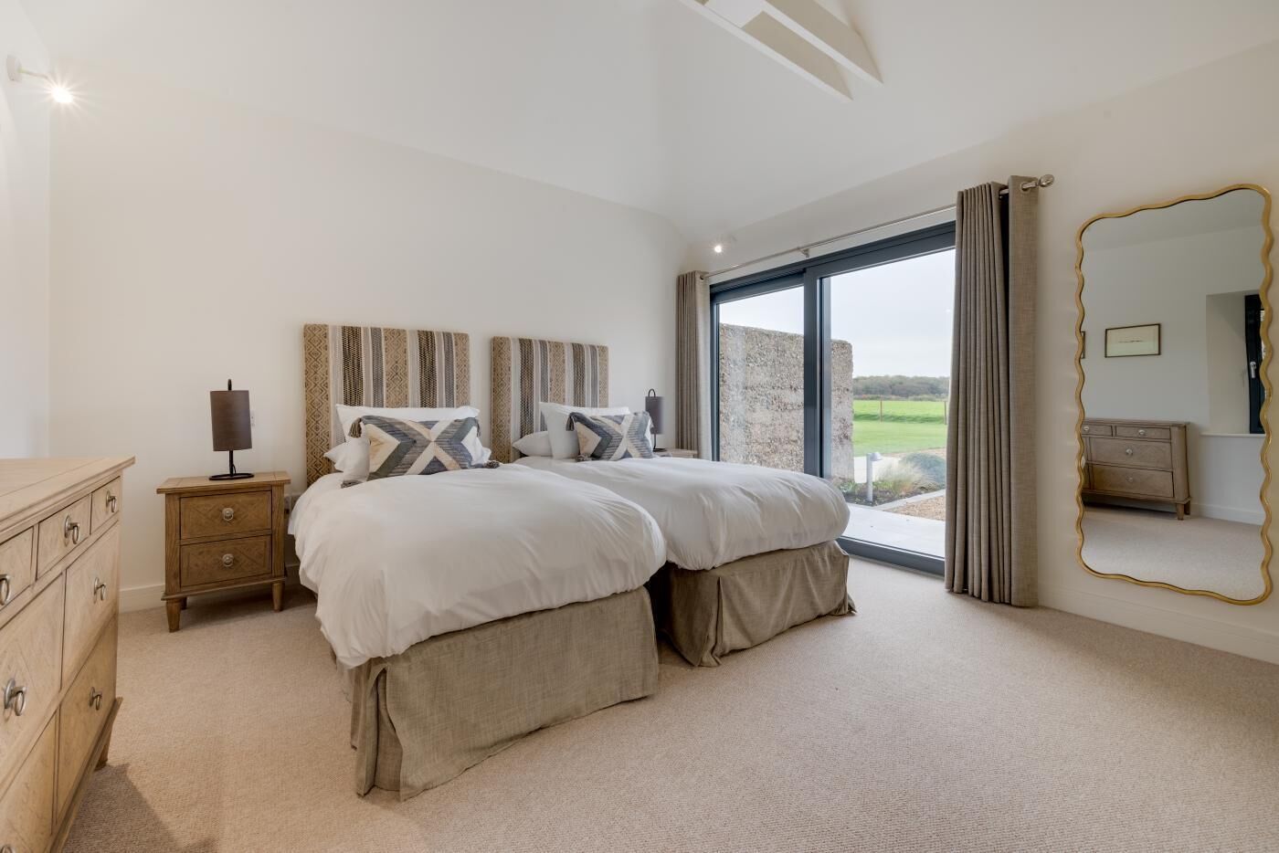 A bedroom with a large bed, a dresser, a mirror, and a view of the outdoors.