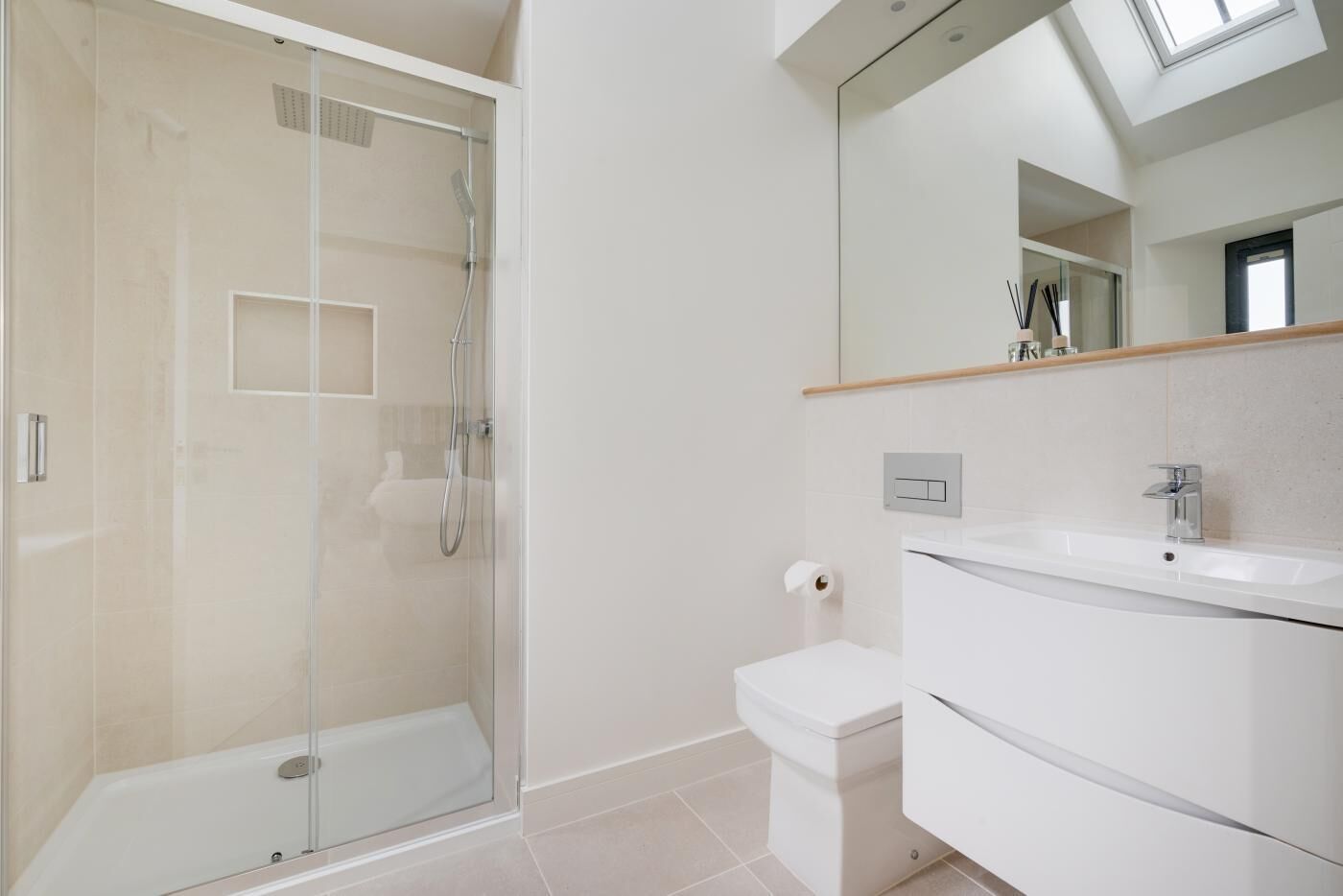 Un bany modern amb dutxa protegida per vidre, un vàter blanc i un lavabo amb mirall.