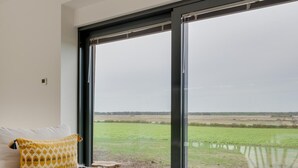 Une chambre avec une grande fenêtre, un lit recouvert d’une couverture moelleuse et un oreiller jaune.
