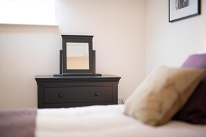 Ein Bett mit weißer Decke und einem dunkelbraunen Nachttisch mit Spiegel und einer Schublade.